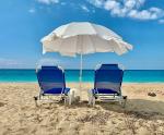 Piaszczysta plaża. Na plaży dwa leżaki pod parasolem.